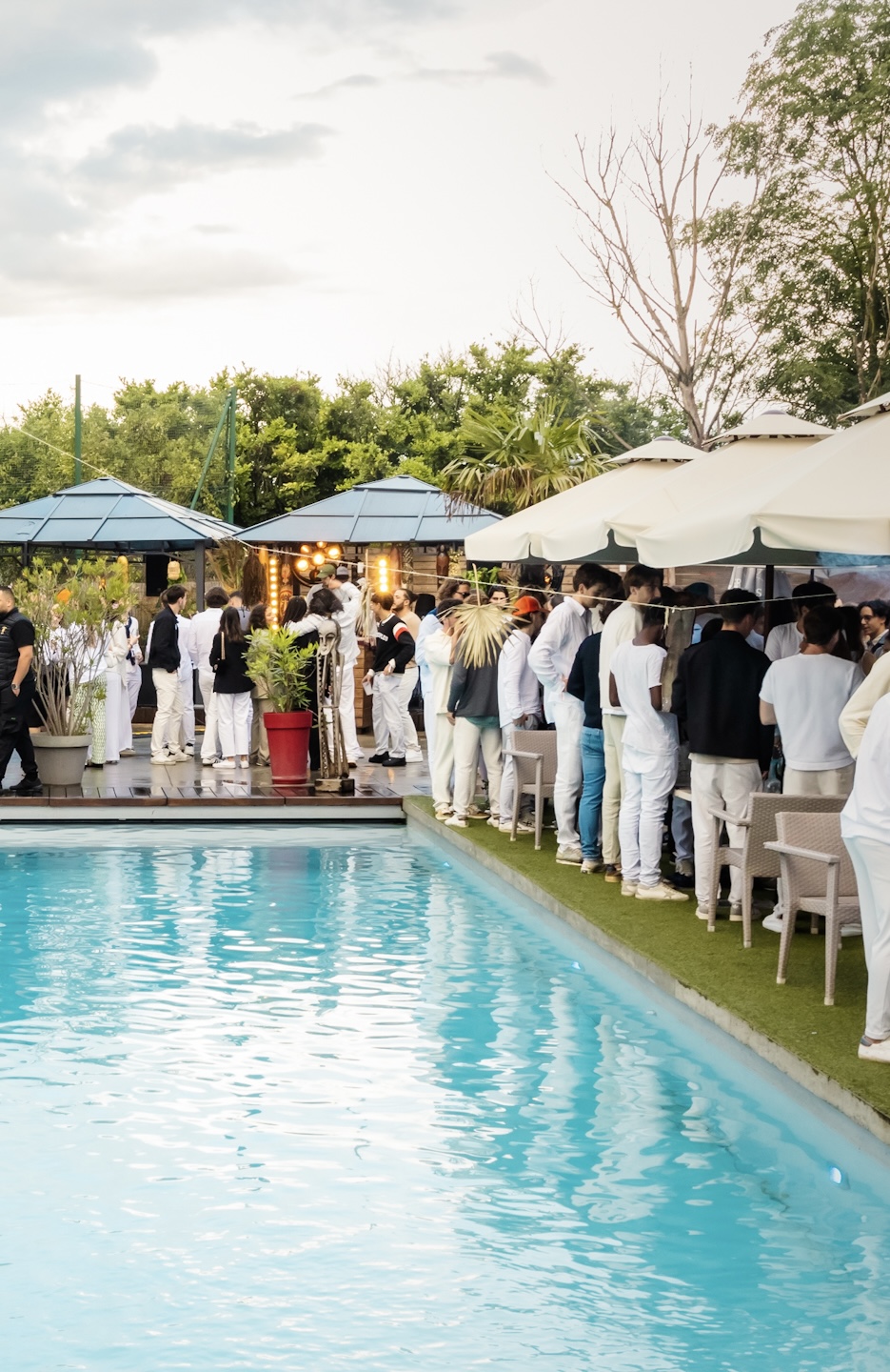 Soirée pool party chic en extérieur avec invités habillés en blanc, ambiance festive près d'une piscine en journée.