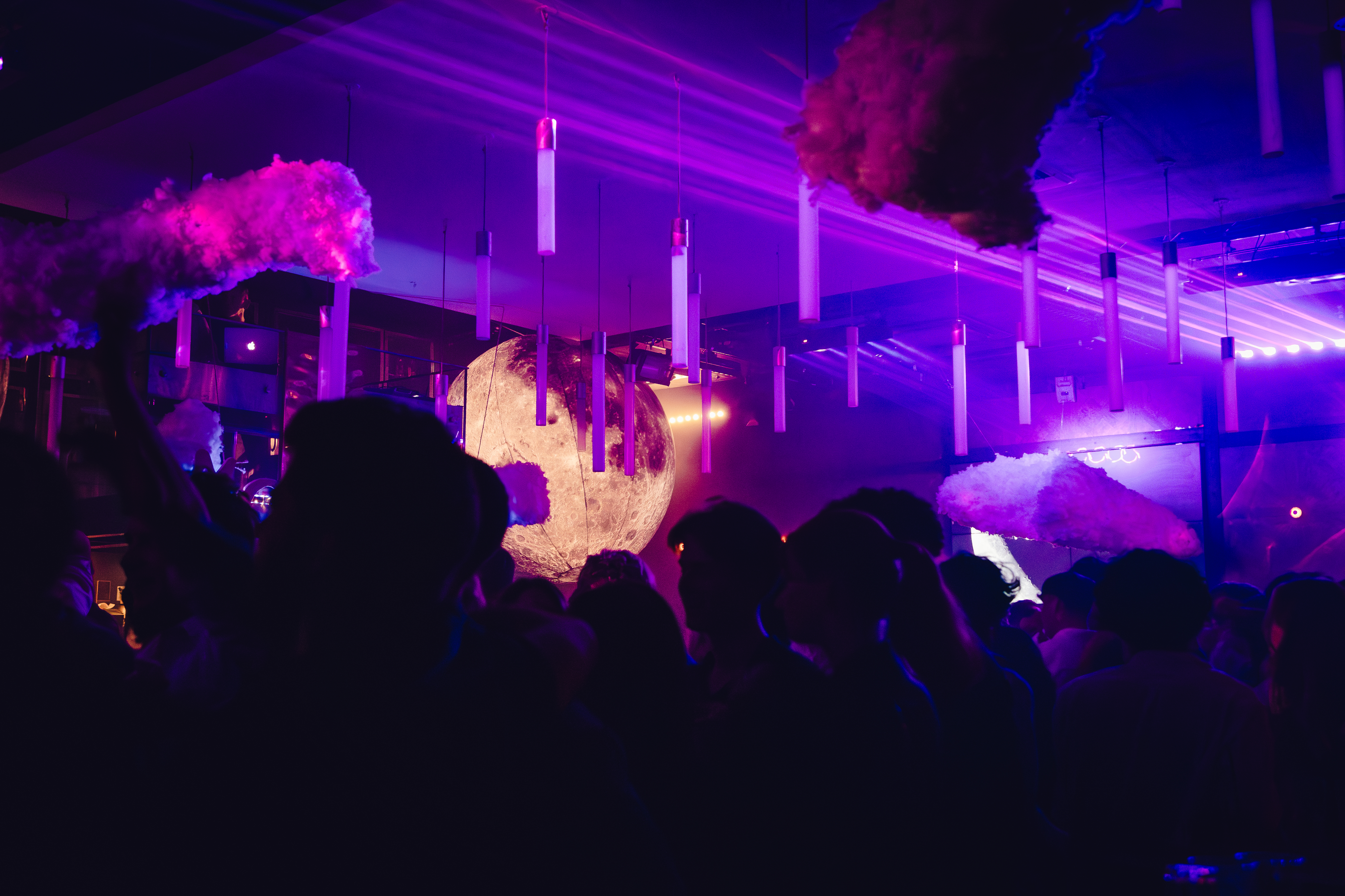 Ambiance immersive dans une boîte de nuit violette, avec des nuages suspendus et une grande sphère lunaire illuminée au centre du plafond.