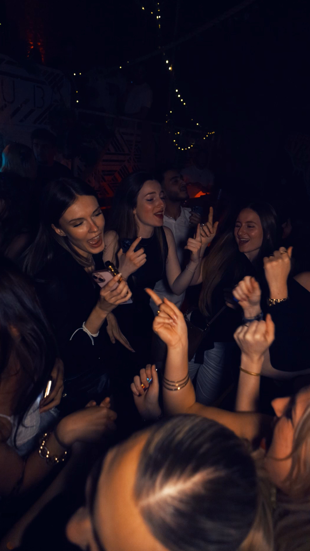 Groupe de jeunes femmes dansant et chantant en club, ambiance festive et conviviale.