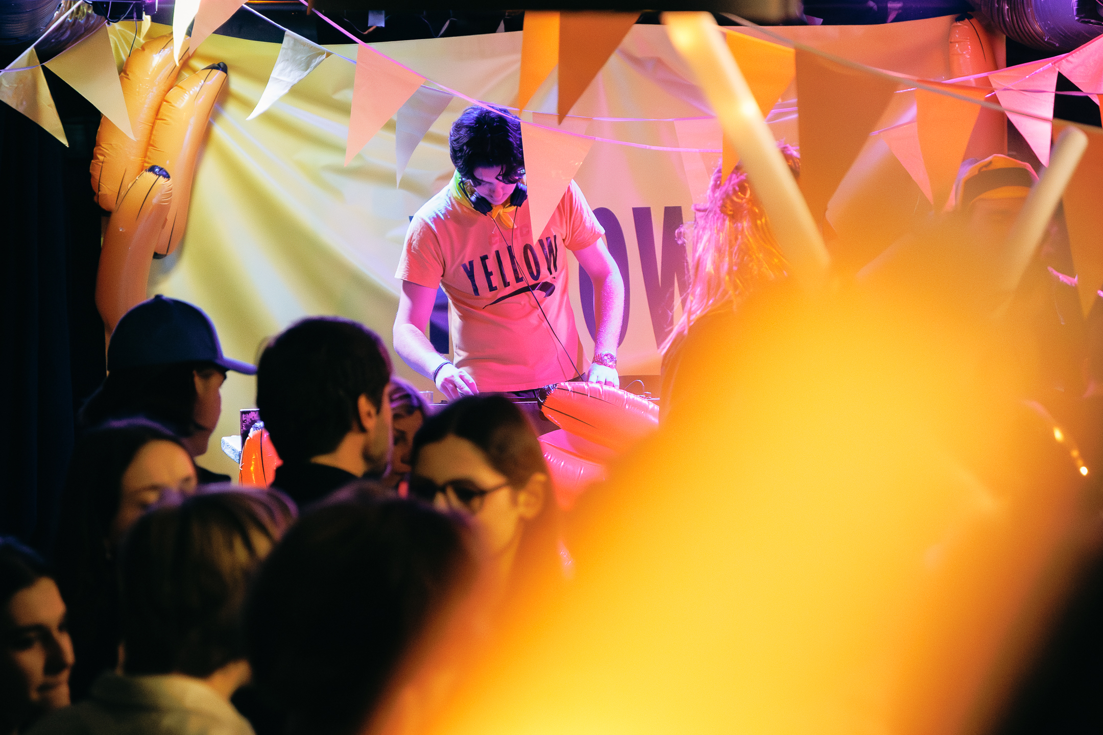 DJ aux platins avec un tshirt jaune sur lequel est écrit YELLOW, en fond une bannière Yellow, des bananes et au plafond des drapeaux jaunes.